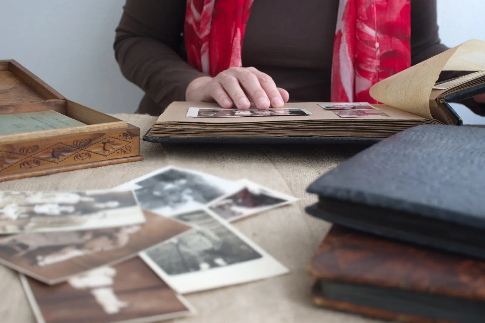 Person blättert in einem alten Fotoalbum, davor lose Schwarzweißabzüge auf dem Tisch
