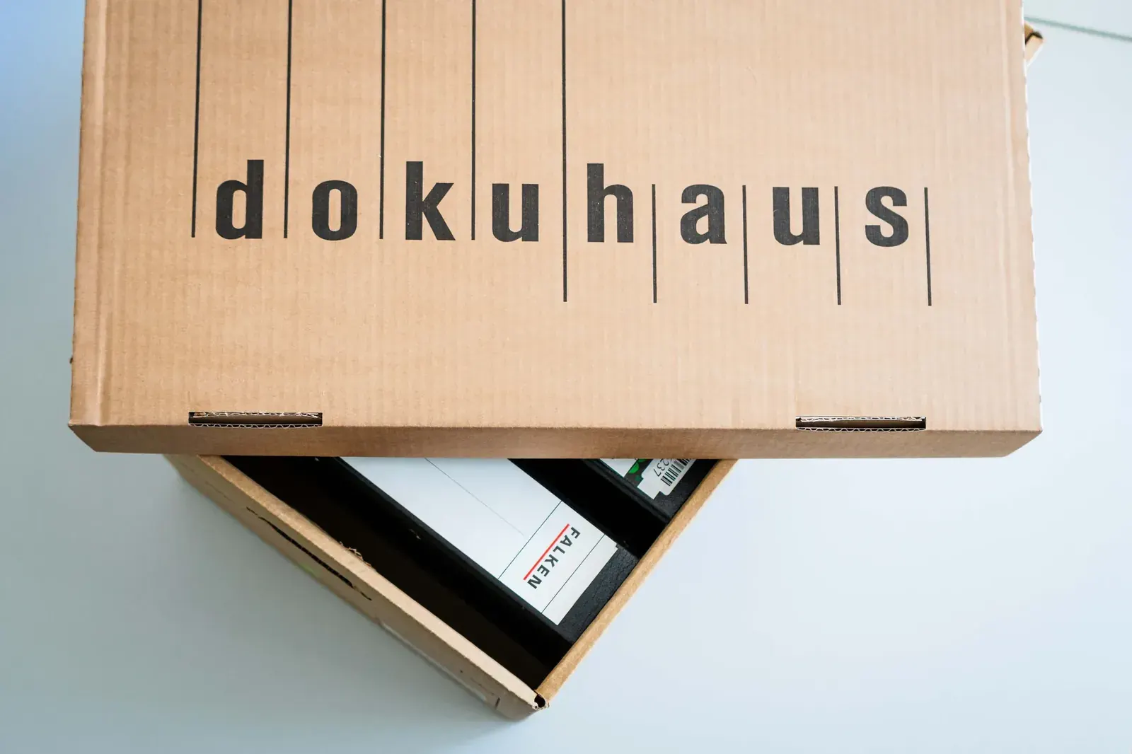 Halb geöffneter dokuhaus-Archivkarton mit Aktenordnern